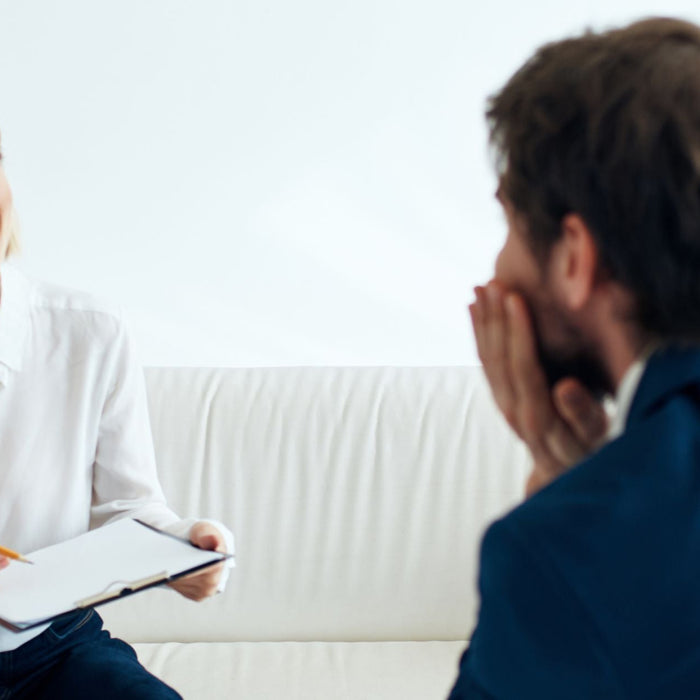Young female therapist holding a clipboard and pencil, smiling as she listens to a male client sitting across from her on a white couch.