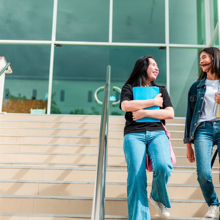 2 college students walking down the stairs on their campus, carrying books and backpacks.