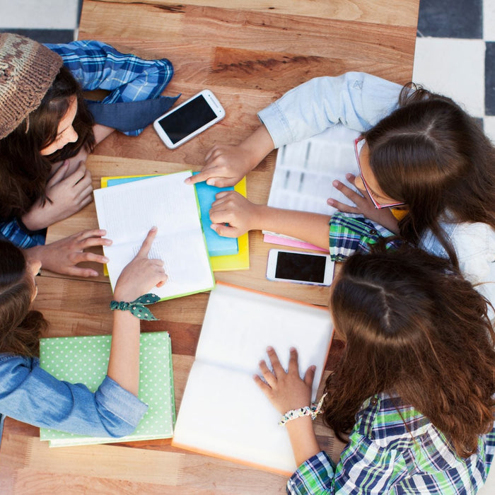 Group of four students reading and pointing to a page of a book