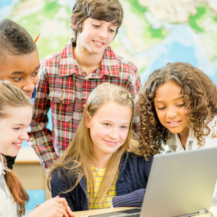 A group of students standing together looking over 1 laptop