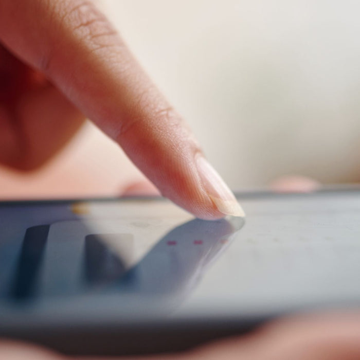 Close-up of a finger tapping on a smartphone screen, with a blurred interface visible beneath the touch. The image highlights mobile interaction and touchscreen technology in use.
