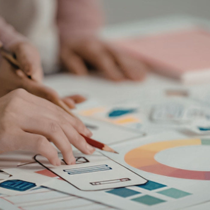 Close-up of hands using a pencil to sketch interface elements and review colorful charts and graphs on paper, suggesting UX design or data visualization planning.