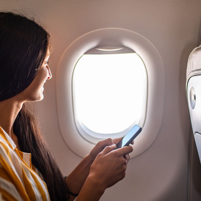 autistic adult on their phone while sitting in the window seat on a plane.